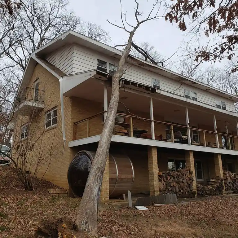 Large tree severely tilting against a two-story house