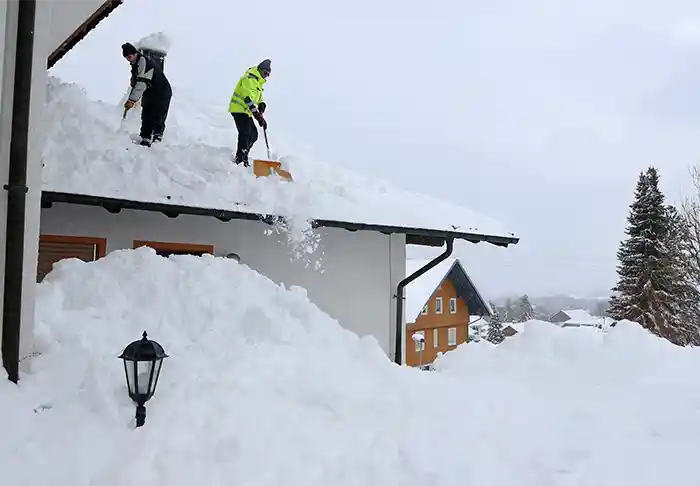 Two men shoveling snow off of a roof